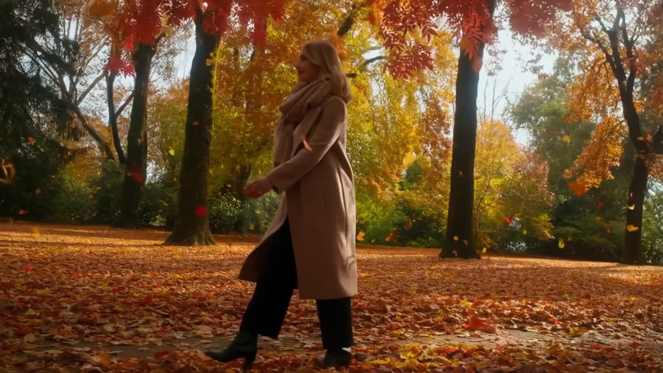 A woman walks through a park with leaves falling around her